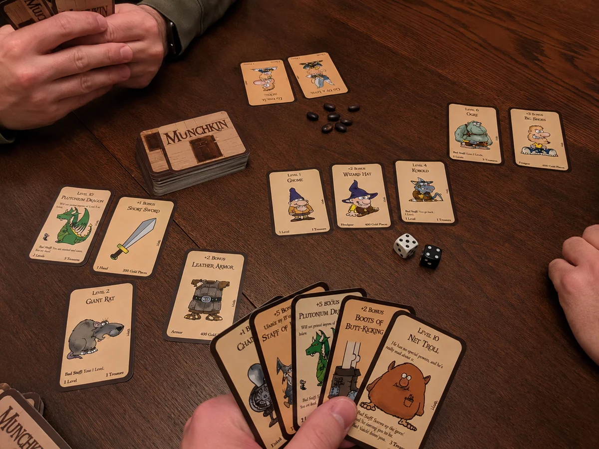 Mãos de jogadores durante uma partida de Munchkin com cartas, dados e marcadores sobre a mesa