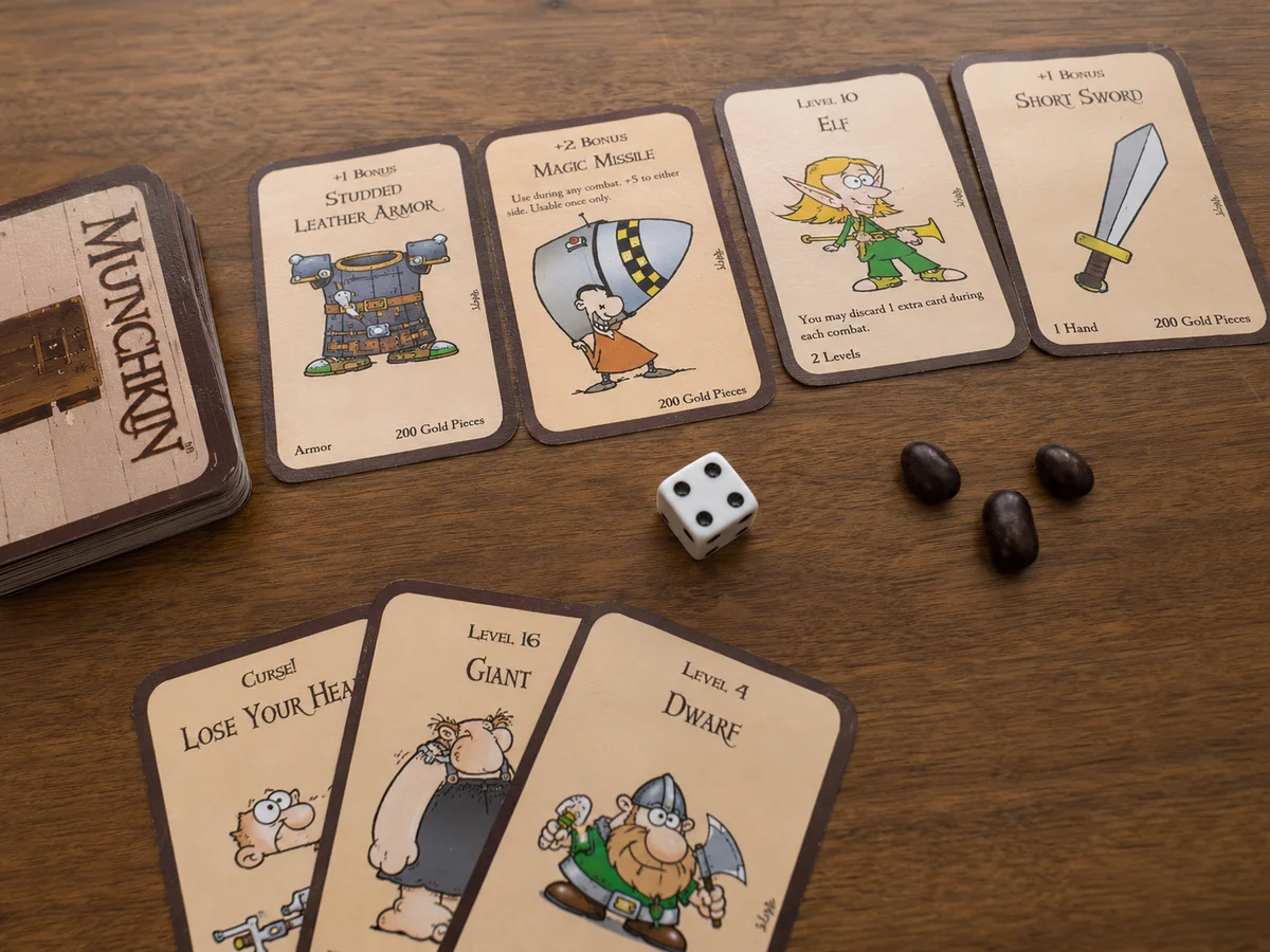 Cartas de Munchkin organizadas sobre a mesa com dado de seis lados e marcadores de nível